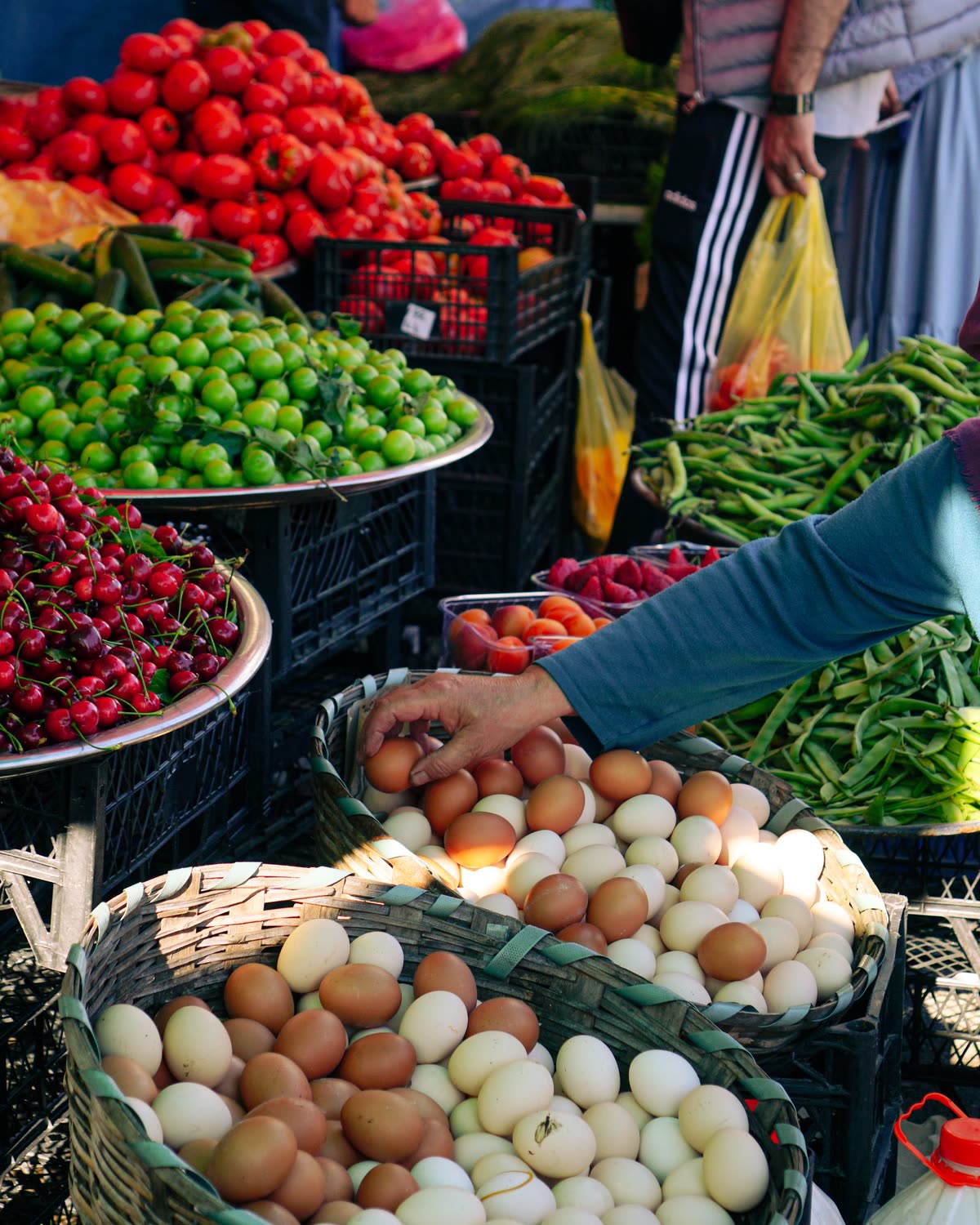 Étal de marché : cageots de légumes et une main choisissant des œufs fermiers